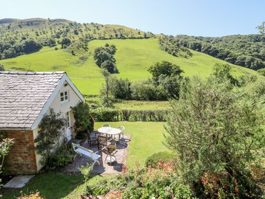A garden with patio furniture and a small house near green hills at Dolgenau Hir - The Barn Llawr y Glyn near Trefeglwys