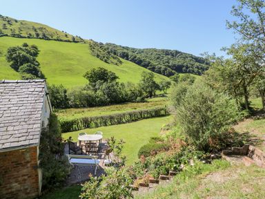 A garden area with outdoor table and chairs near hills and trees at Dolgenau Hir - The Barn in Llawr y Glyn near Trefeglwys