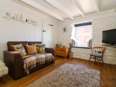 A living room with a brown leather sofa a wooden chest a window with cushions a wooden chair and a wall-mounted tv at Ner Sea in Marazion