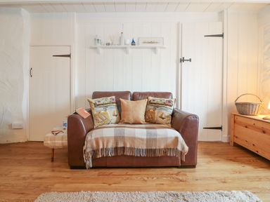 A brown leather sofa with three cushions and a plaid throw in a room with white paneled walls and wooden floor at Ner Sea in Marazion