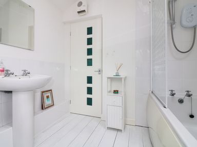 A bathroom with a white sink a small cabinet a bathtub with shower unit and a door with glass panels at Ner Sea in Marazion