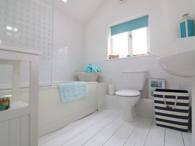A bathroom with a bathtub a toilet a sink a basket with towels and a striped laundry basket at Ner Sea in Marazion