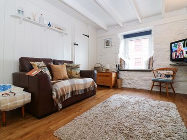 A living room with a brown leather sofa wooden chair and a mounted television at Ner Sea in Marazion