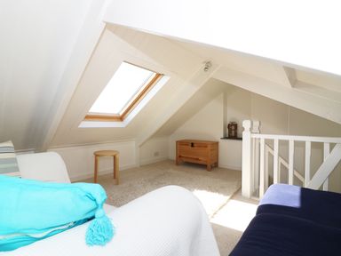 A small attic room with a skylight window a wooden stool a wooden chest and seating at Ner Sea in Marazion