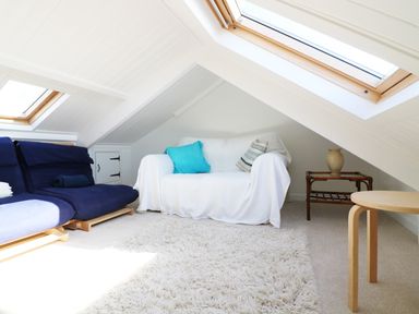 A living area under a slanted ceiling with blue and white sofas a small table with a vase and skylights at Ner Sea in Marazion