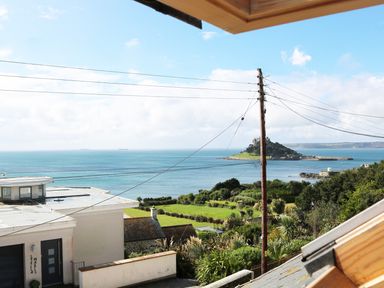 A coastal view with houses greenery a utility pole and an island with a castle at Ner Sea in Marazion