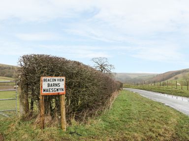 A rural road beside a hedge and a sign reading Beacon View Barns Maesgwyn at 1 Beacon View Barn in Beguildy near Knighton