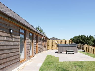 A wooden exterior wall with windows and a fenced patio area with a hot tub at 1 Beacon View Barn in Beguildy near Knighton