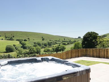 An outdoor hot tub on a patio overlooking green hills and trees at 1 Beacon View Barn in Beguildy near Knighton