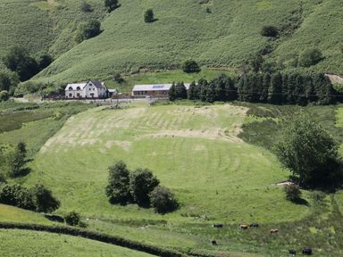 A farmhouse and barn near a grassy field with cows and trees at 1 Beacon View Barn in Beguildy near Knighton