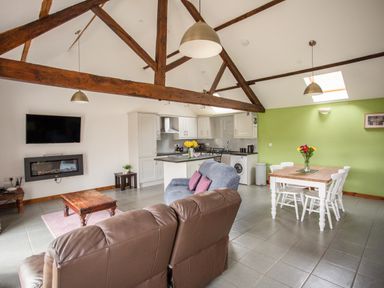 An open living area with wooden beams a kitchen dining table with flowers and a sitting area at 1 Beacon View Barn in Beguildy near Knighton
