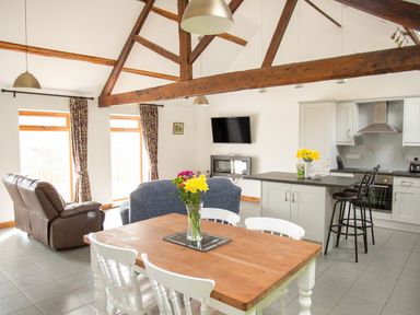 A kitchen dining and living area with wooden beams wooden dining table white chairs and a wall mounted TV at 1 Beacon View Barn Beguildy near Knighton