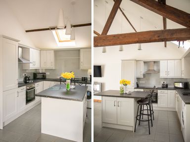A kitchen with white cabinets black countertops a central island with flowers and wooden beams on the ceiling at 1 Beacon View Barn in Beguildy near Knighton