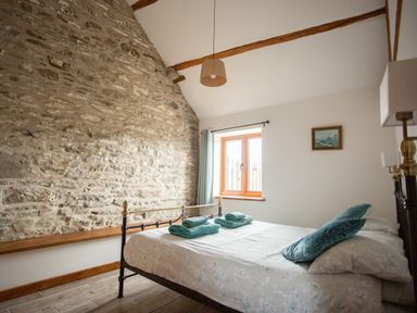 A bedroom with a stone wall a window a bed with pillows and towels at 1 Beacon View Barn in Beguildy near Knighton