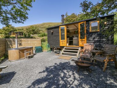 A black wooden shepherds hut with open doors leading to a kitchen area outside seating and a wooden hot tub at Moelfre - Shepherds Hut in Llanbedr