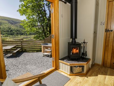 A wood burning stove near an open door leading to an outdoor area with a picnic table and hot tub at Moelfre - Shepherds Hut in Llanbedr