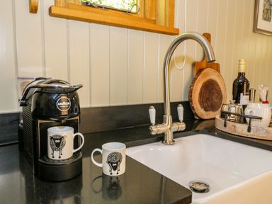 A kitchen sink with a modern faucet a coffee machine with two mugs and a tray with bottles and cups on the counter at Moelfre - Shepherds Hut in Llanbedr