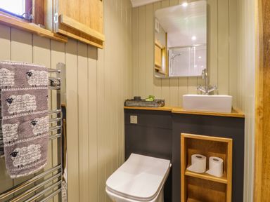 A small bathroom with a toilet a sink a mirror and a towel rack with sheep patterned towels at Moelfre - Shepherds Hut in Llanbedr