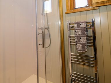 A bathroom shower enclosure with a glass door and a chrome heated towel rail with a sheep patterned towel at Moelfre - Shepherds Hut in Llanbedr