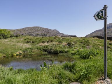 A small pond in a grassy area with hills and a walking signpost at Moelfre - Shepherds Hut in Llanbedr