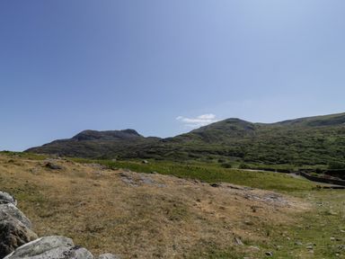 An open landscape with grassy hills and rocky terrain under a clear blue sky at Moelfre - Shepherds Hut in Llanbedr