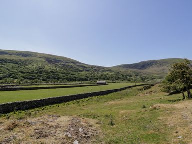 A rural landscape with stone fences green fields and hills under a clear sky at Moelfre - Shepherds Hut in Llanbedr