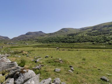 A grassy field with scattered rocks and a dry stone wall with hills in the background at Moelfre - Shepherds Hut in Llanbedr