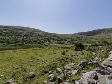 A grassy field with rocks and hills in the background at Moelfre - Shepherds Hut in Llanbedr