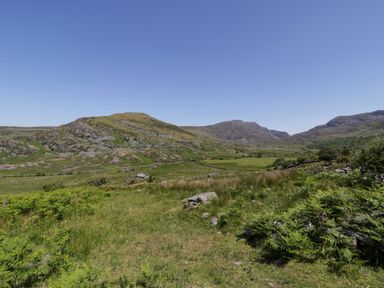 A valley with green grass and rocky hills under a clear blue sky at Moelfre - Shepherds Hut in Llanbedr