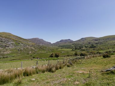 A grassy valley with hills in the background and a wire fence in the foreground at Moelfre - Shepherds Hut in Llanbedr
