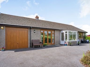 A single story brick house with a wooden garage door wooden framed glass doors a small porch and outdoor seating at Yr Hen Ffald in Pontarddulais