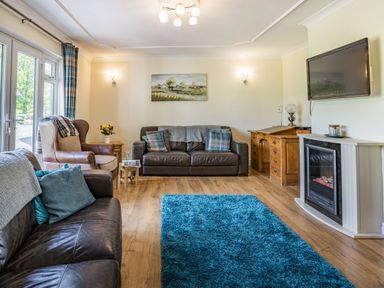 A living room with leather sofas a blue rug a wooden desk and a wall-mounted television at Yr Hen Ffald in Pontarddulais