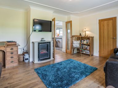 A living room with a blue rug a wall mounted tv a fireplace wooden furniture and an open door at Yr Hen Ffald in Pontarddulais