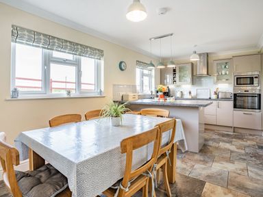 A kitchen with wooden chairs and table with tablecloth and plant at Yr Hen Ffald in Pontarddulais