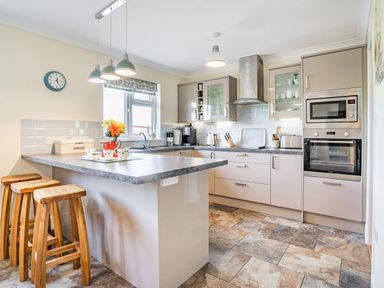 A kitchen with an island counter and three wooden stools at Yr Hen Ffald in Pontarddulais