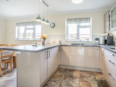 A kitchen with a countertop island chairs a sink cupboards and windows at Yr Hen Ffald in Pontarddulais