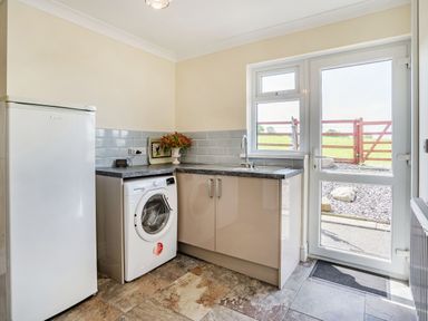 A utility room with a washing machine, refrigerator, sink, countertop, and door leading outside at Yr Hen Ffald in Pontarddulais