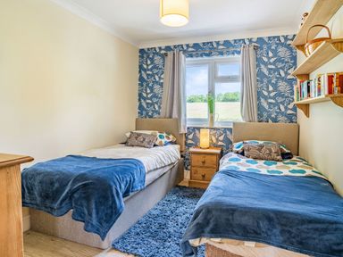 A bedroom with two single beds blue bed covers a window with curtains and a nightstand at Yr Hen Ffald in Pontarddulais