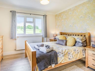A bedroom with a wooden bed frame with floral bedding bedside tables with lamps a window with grey curtains and a chest of drawers at Yr Hen Ffald in Pontarddulais
