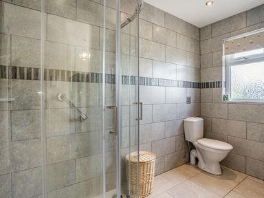 A bathroom with a glass shower enclosure a toilet a wicker laundry basket and a window at Yr Hen Ffald in Pontarddulais