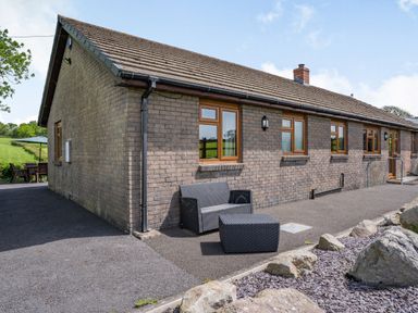 An outdoor patio area with a bench and table next to a brick building with multiple windows at Yr Hen Ffald in Pontarddulais