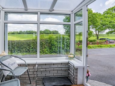 A small enclosed porch with chairs a shoe rack and a view of a green field at Yr Hen Ffald in Pontarddulais