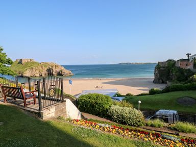 A garden with flowers and a bench overlooking a sandy beach and the ocean at The Shell at the Hideaway Tenby