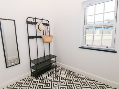 A hallway with a black bench and coat rack a mirror on the wall and a window at The Shell at the Hideaway in Tenby