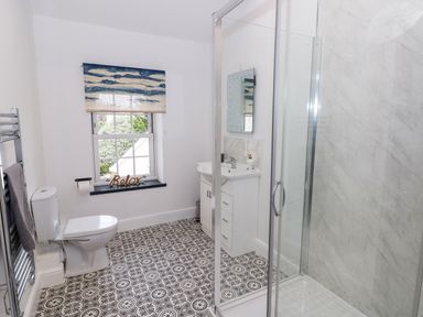 A bathroom with toilet towel rack shower sink and a window with patterned floor at The Shell at the Hideaway in Tenby