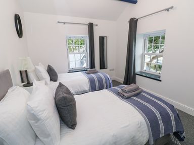 A bedroom with two single beds gray pillows and blue striped throws at The Shell at the Hideaway in Tenby