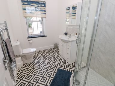 A bathroom with a toilet a sink with a vanity mirror a shower and a window with a blind at The Shell at the Hideaway in Tenby