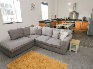 An open living room and kitchen with a gray sectional sofa and wooden cabinets at The Shell at the Hideaway in Tenby