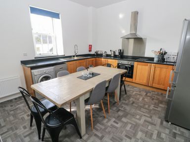 A kitchen with wooden cabinets a dining table with chairs and appliances at The Shell at the Hideaway in Tenby