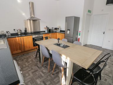 A kitchen with a wooden dining table and mixed chairs near wooden cabinets and a stainless steel refrigerator at The Shell at the Hideaway in Tenby